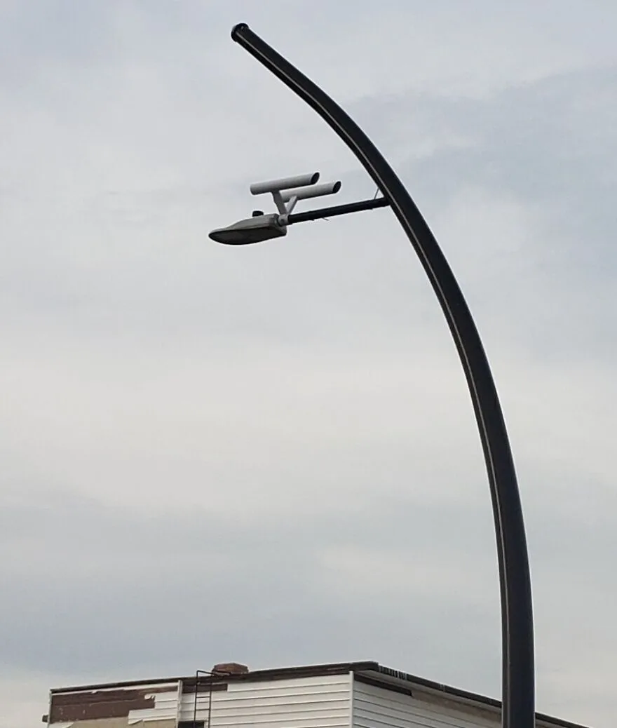 A streetlight with a curved black pole and a lamp head that is shaped like the iconic saucer and nacelles of a starship from…