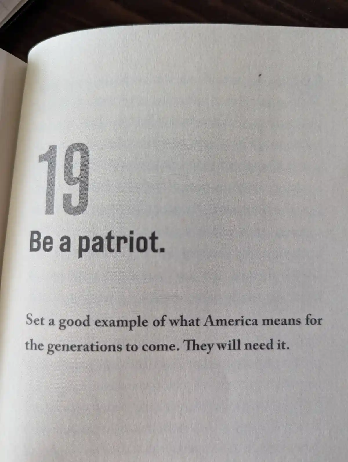 A close-up of a book page showing the number 19, followed by the text 'Be a patriot.' and the subtext 'Set a good example of…
