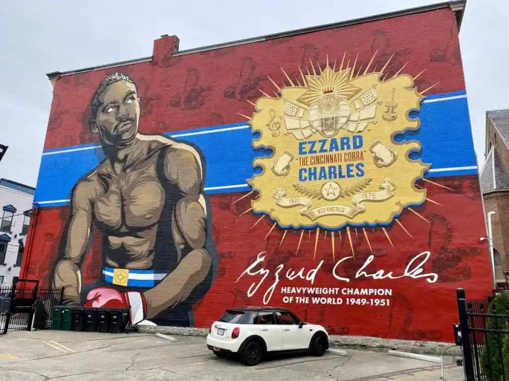 A large mural on a red brick building depicts boxer Ezzard 'The Cincinnati Cobra' Charles, showing him shirtless with boxing…
