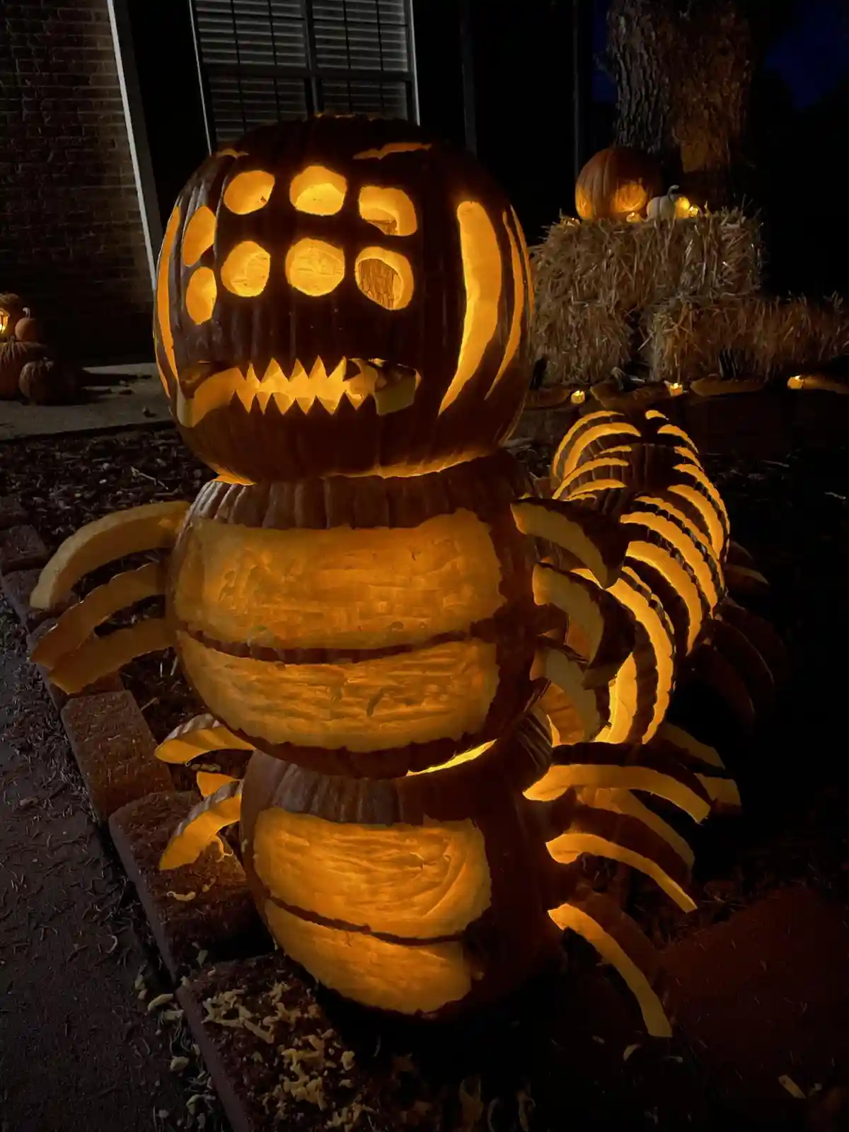 A large, intricately carved Halloween pumpkin sculpture shaped like a multi-legged creature, possibly a centipede or…