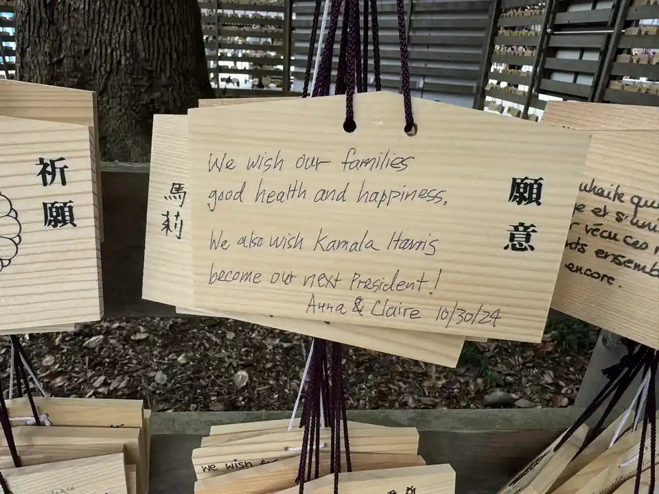 A wooden Japanese prayer plaque (ema) hangs among others at a shrine, featuring handwritten English text wishing family…