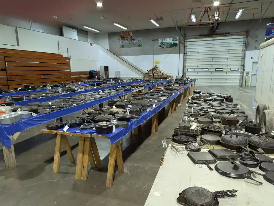 A large indoor space, likely a warehouse or auction hall, is filled with long tables covered in blue tarps displaying…