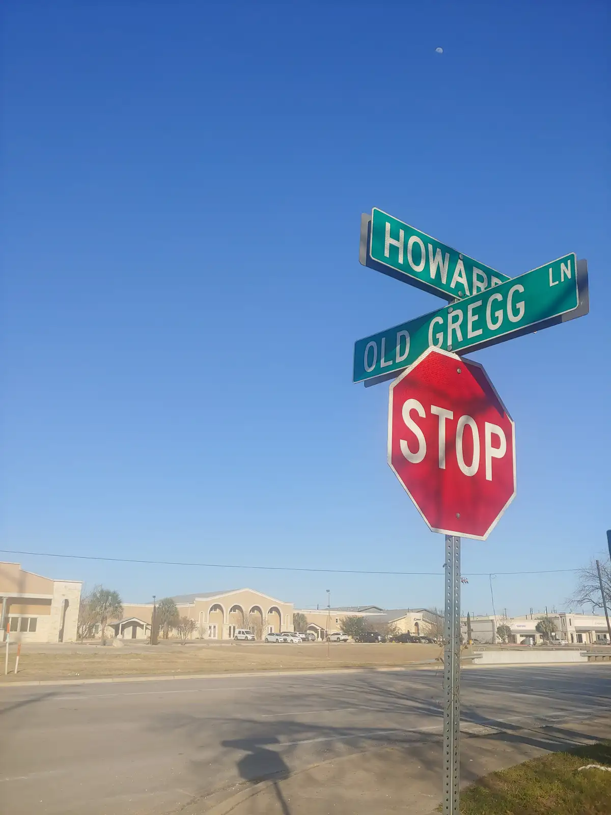 A red octagonal stop sign is mounted below two green street signs reading 'HOWARD' and 'OLD GREGG LN', set against a clear…