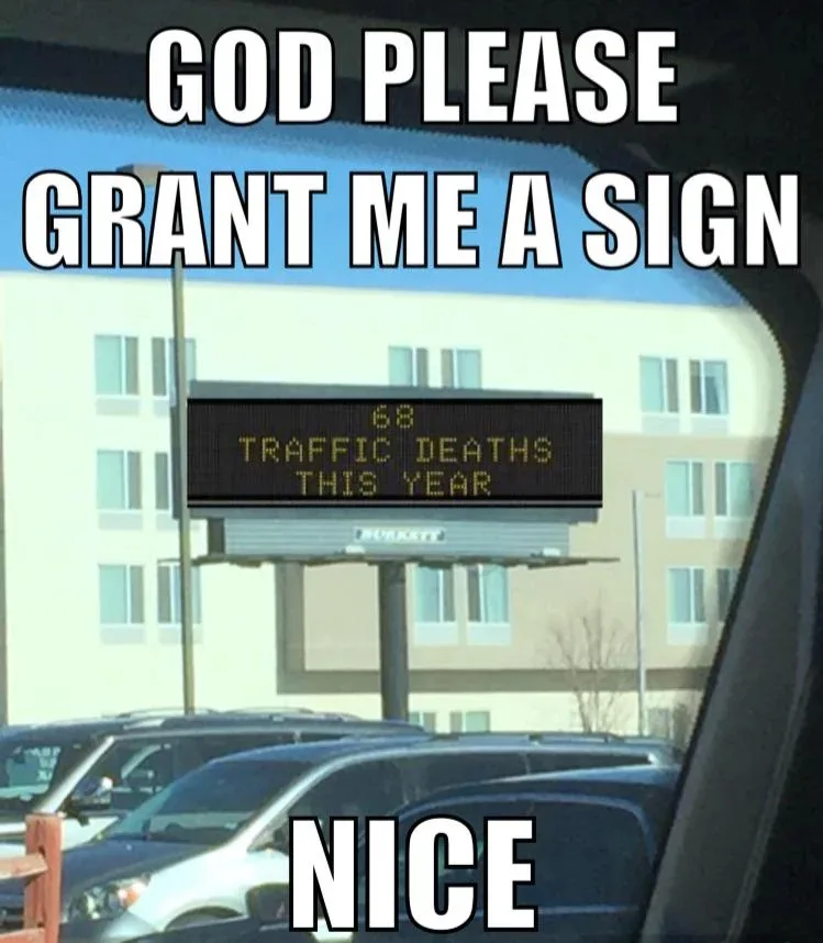 A photo taken from inside a car shows a roadside electronic sign displaying '68 TRAFFIC DEATHS THIS YEAR'. The image is…