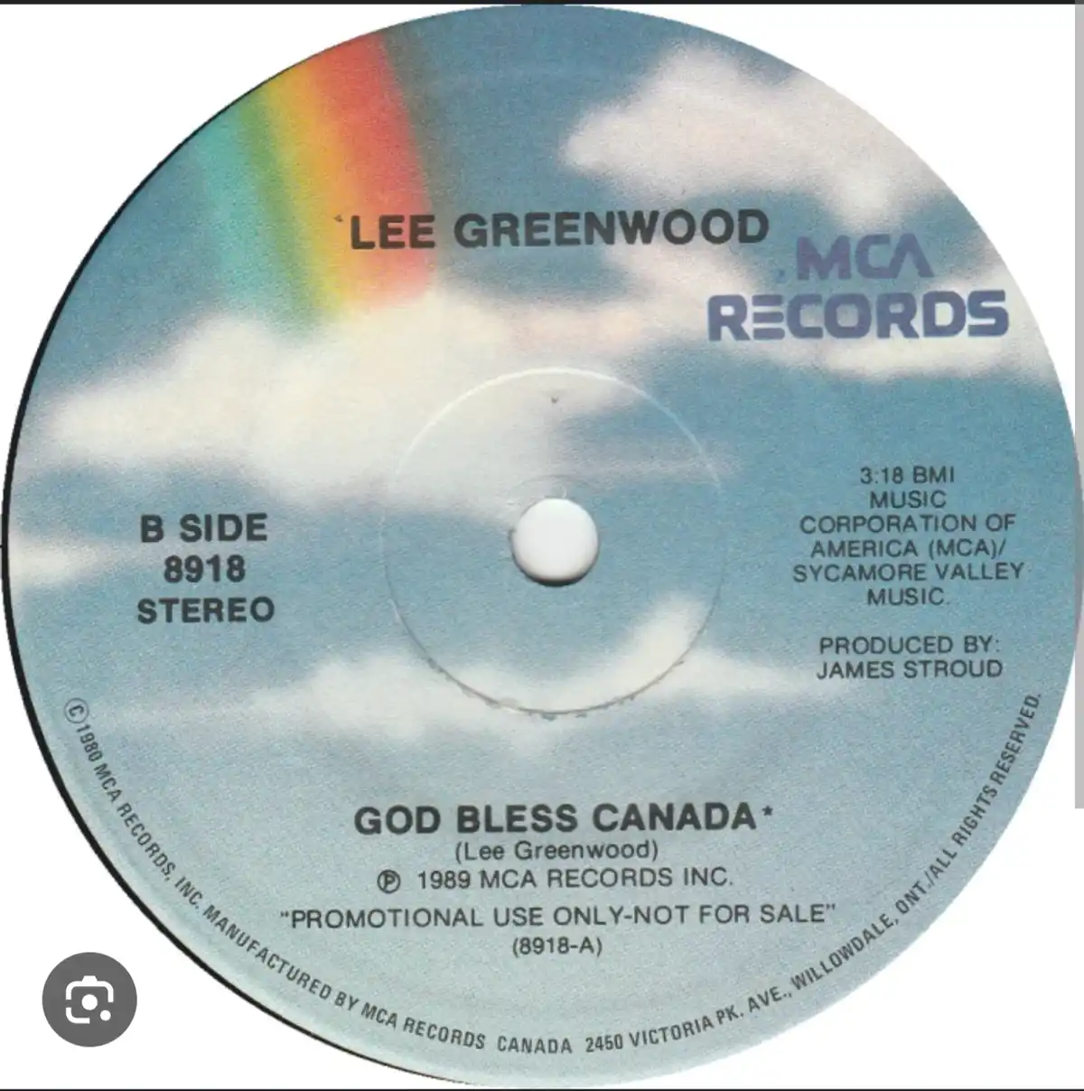 A close-up of a promotional vinyl record label for Lee Greenwood's song 'God Bless Canada,' showing the artist name, record…