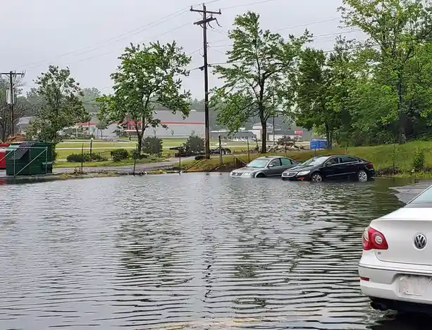 A flooded parking lot shows several cars partially submerged in water, with a silver and black sedan visible in the middle…