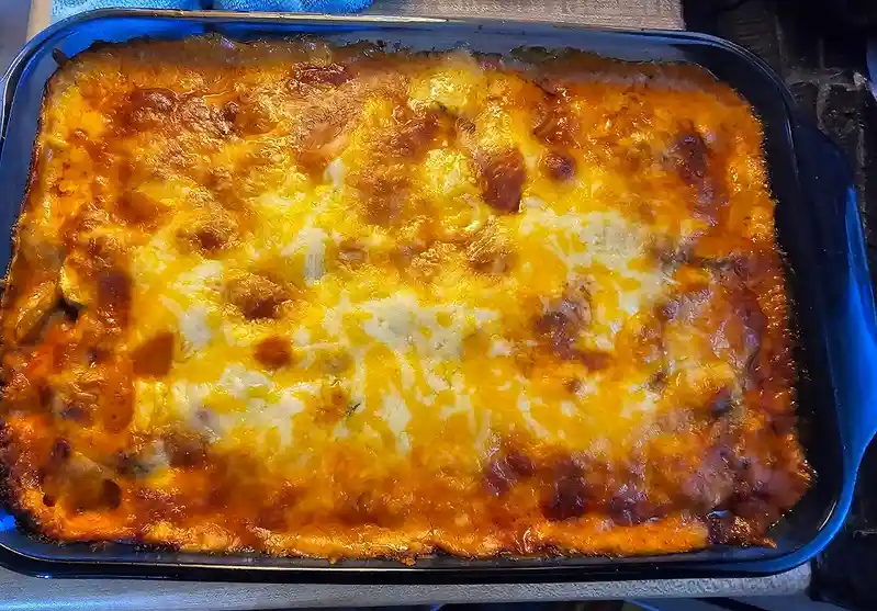 A close-up photo of a rectangular blue baking dish containing a freshly baked lasagna with a golden-brown, bubbly cheese…