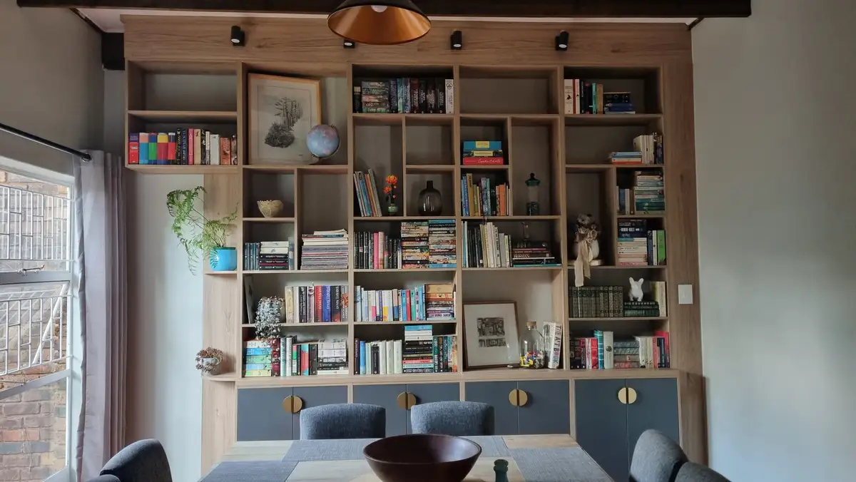 A large, custom-built wooden bookshelf filled with numerous books, decorative items like a globe, framed art, and plants…