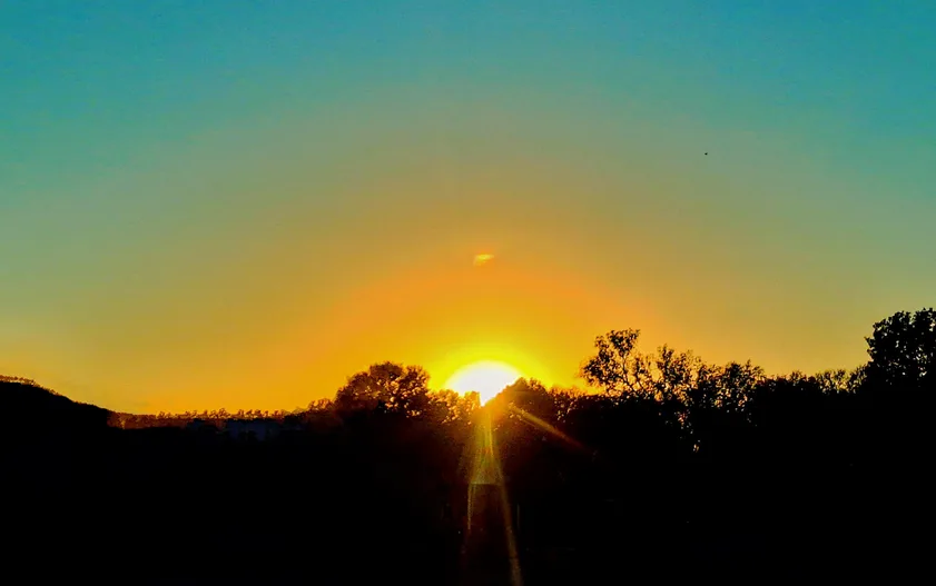 A photograph of a sunrise or sunset with the sun low on the horizon, casting a bright orange glow across the sky…