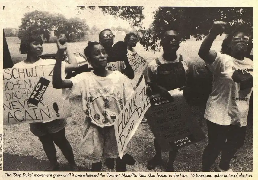A black-and-white photo shows a group of protesters holding signs with messages like 'NO DUKES', 'HONK TO DUMP DUKE', and…
