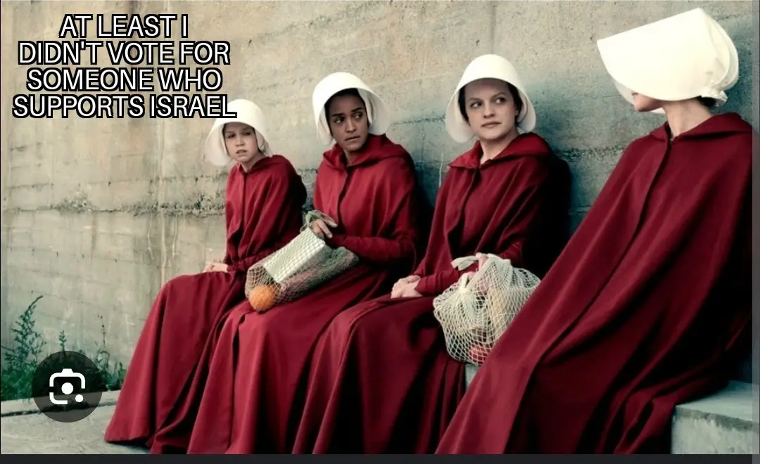 Four women in red robes and white bonnets sit against a concrete wall, looking somber or annoyed. The text overlaid in the…