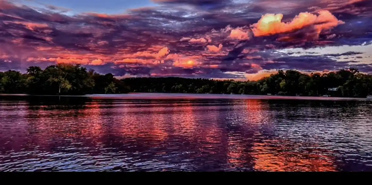 A serene landscape photo of a lake at sunset, with vibrant pink, orange, and purple clouds reflected in the rippling water…