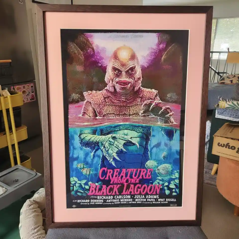 A framed poster for the 1954 movie 'Creature from the Black Lagoon' is displayed in a living room. The poster features the…