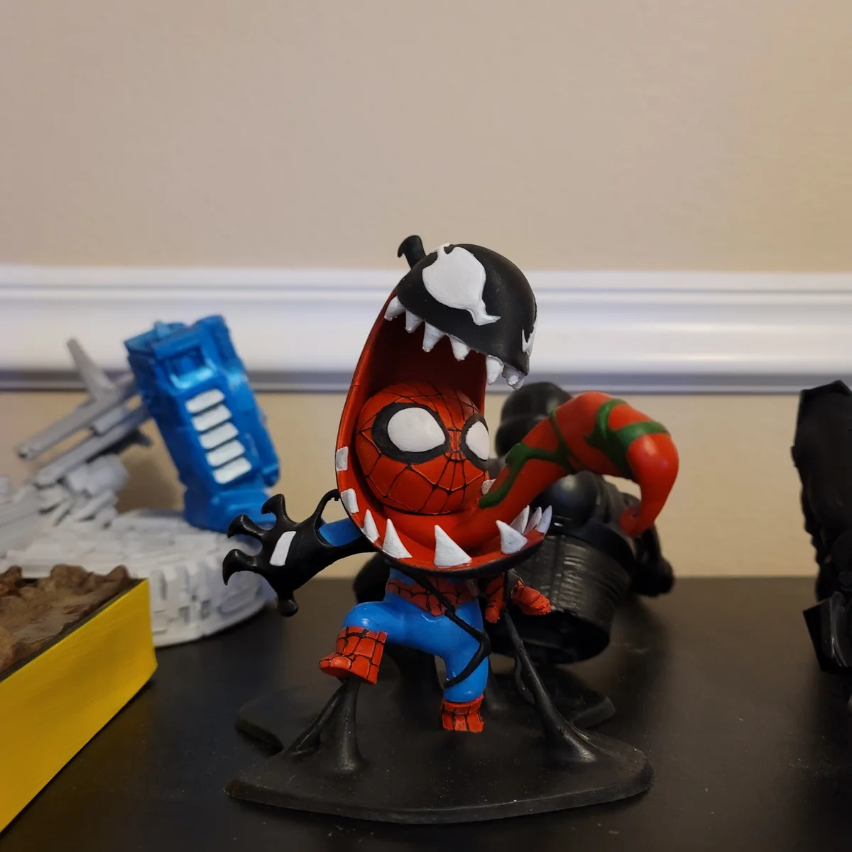 A custom-painted Spider-Man figurine has a Venom symbiote head and mouthpiece, with Venom's black and white face and fangs…