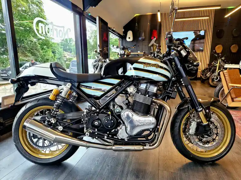 A Norton Commando 961 LE motorcycle is displayed indoors in a showroom with wooden floors and large windows. The bike…