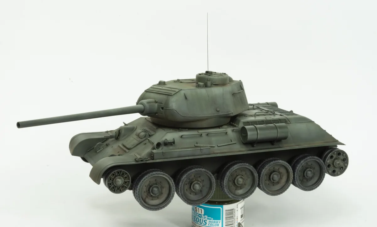 A detailed green model tank is displayed on top of a paint can, with the tank's color matching the paint can's label. The…