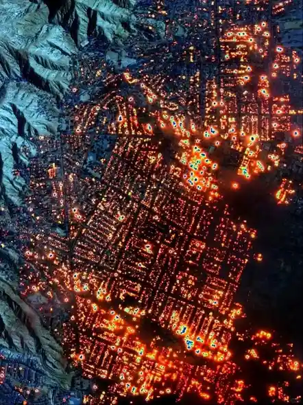 An aerial night view of a densely populated city nestled in mountainous terrain, with countless bright orange and yellow…