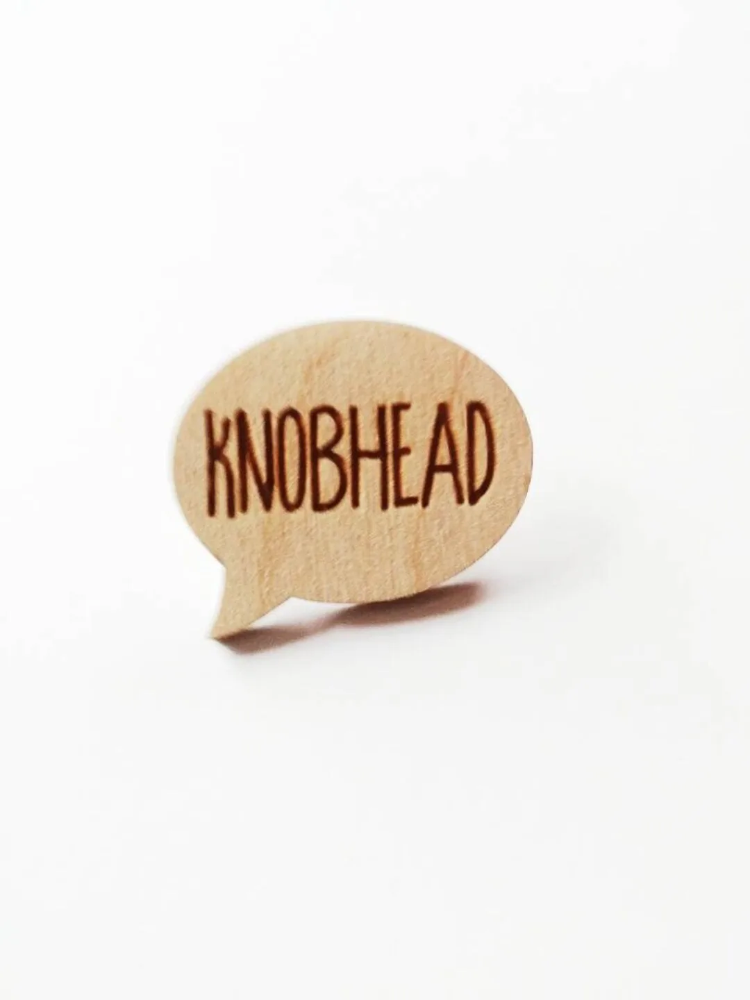 A small, light-colored wooden cutout shaped like a speech bubble stands upright on a plain white surface. The word…