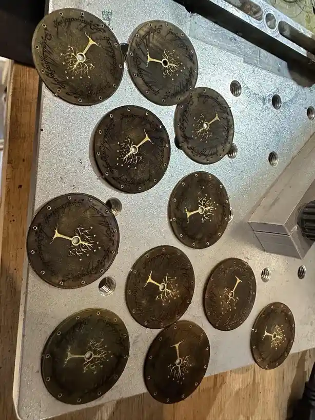 A collection of circular metal discs, each engraved with the Tree of Gondor symbol and surrounded by elvish script, are…