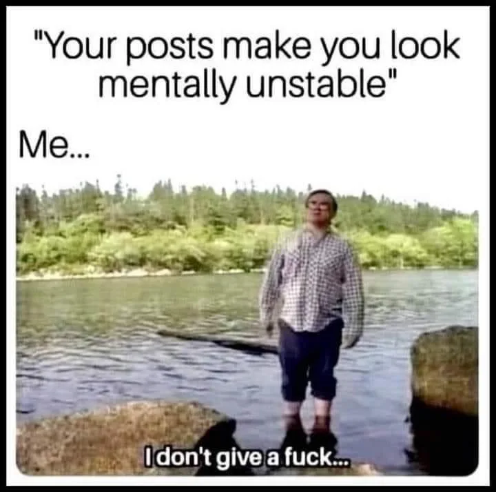 A person stands in shallow water near rocks with a forested shoreline behind them, looking calm and unbothered. The image…