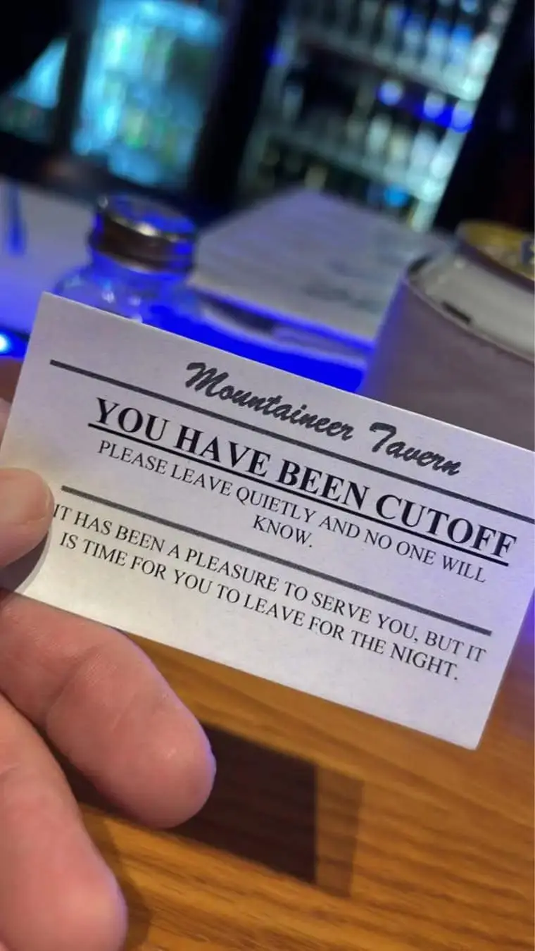 A hand holds a white card from 'Mountaineer Tavern' with bold text stating 'YOU HAVE BEEN CUTOFF' and a polite message…