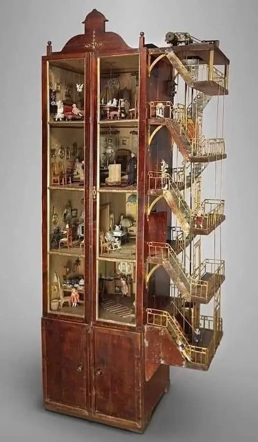 a tall, antique wooden cabinet with glass doors reveals a detailed dollhouse interior with miniature furniture and figures…