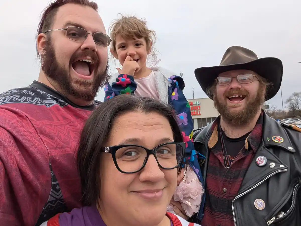 A selfie of four people outdoors, including a woman in the foreground with glasses smiling slightly while looking away, a…