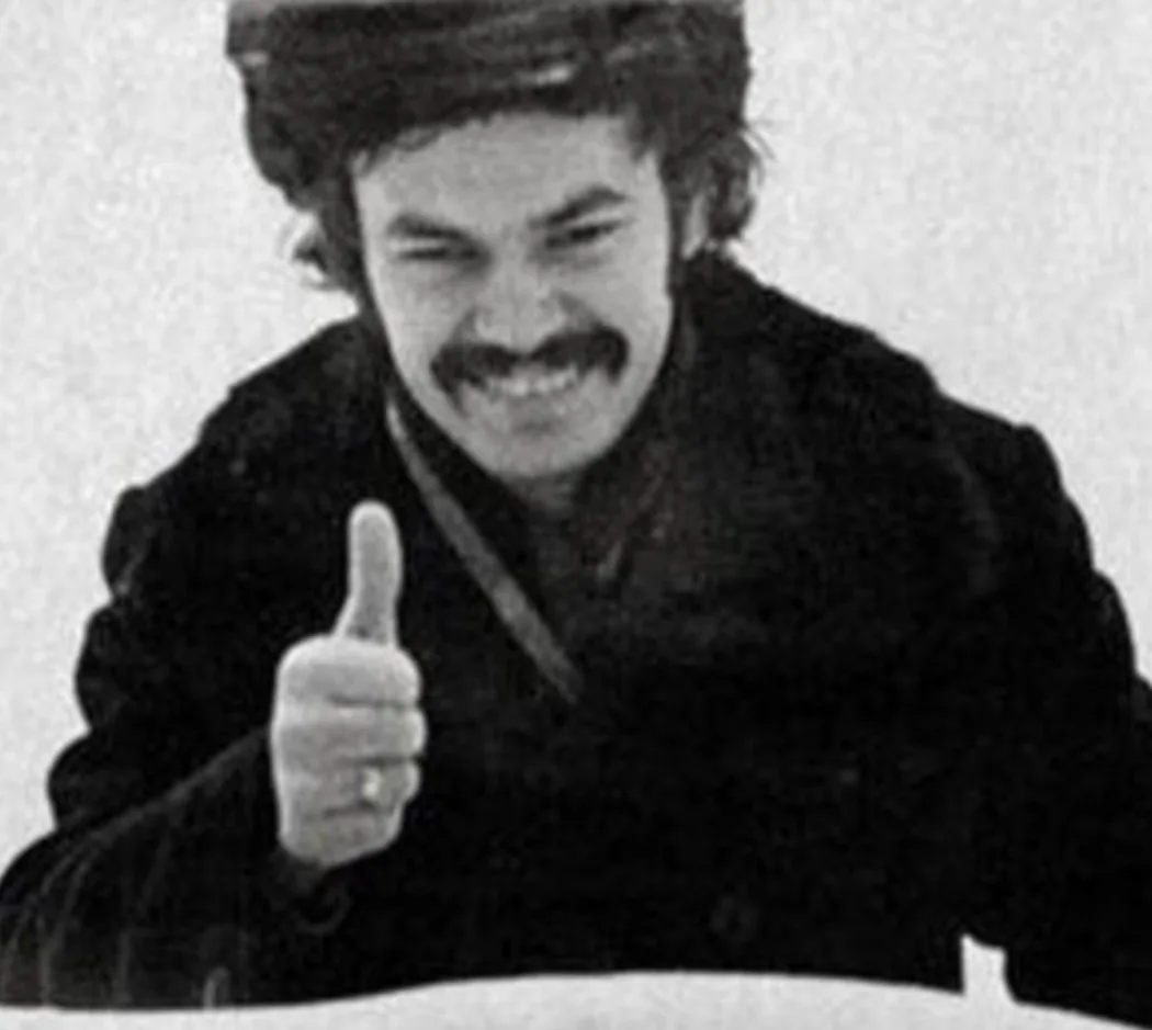 a black and white photo of a man with a mustache and dark hair giving a thumbs-up gesture while smiling. The overlaid text…