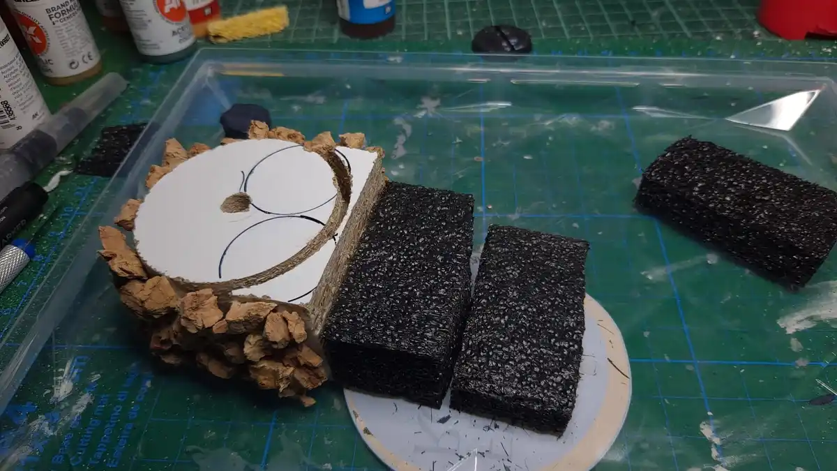 A DIY craft project on a green cutting mat shows a circular white base with cork-like material glued around its edge…