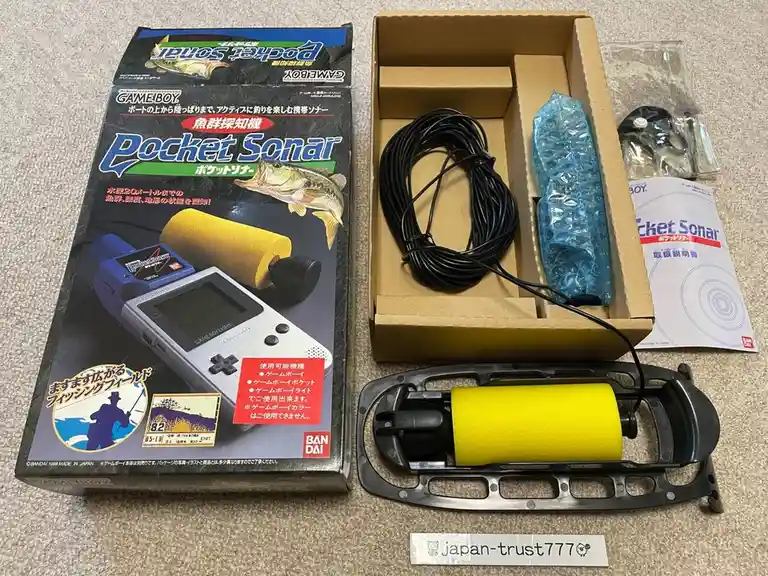 A Game Boy Pocket Sonar fishing sonar device by Bandai, shown with its box, contents including a black cable, bubble-wrapped…