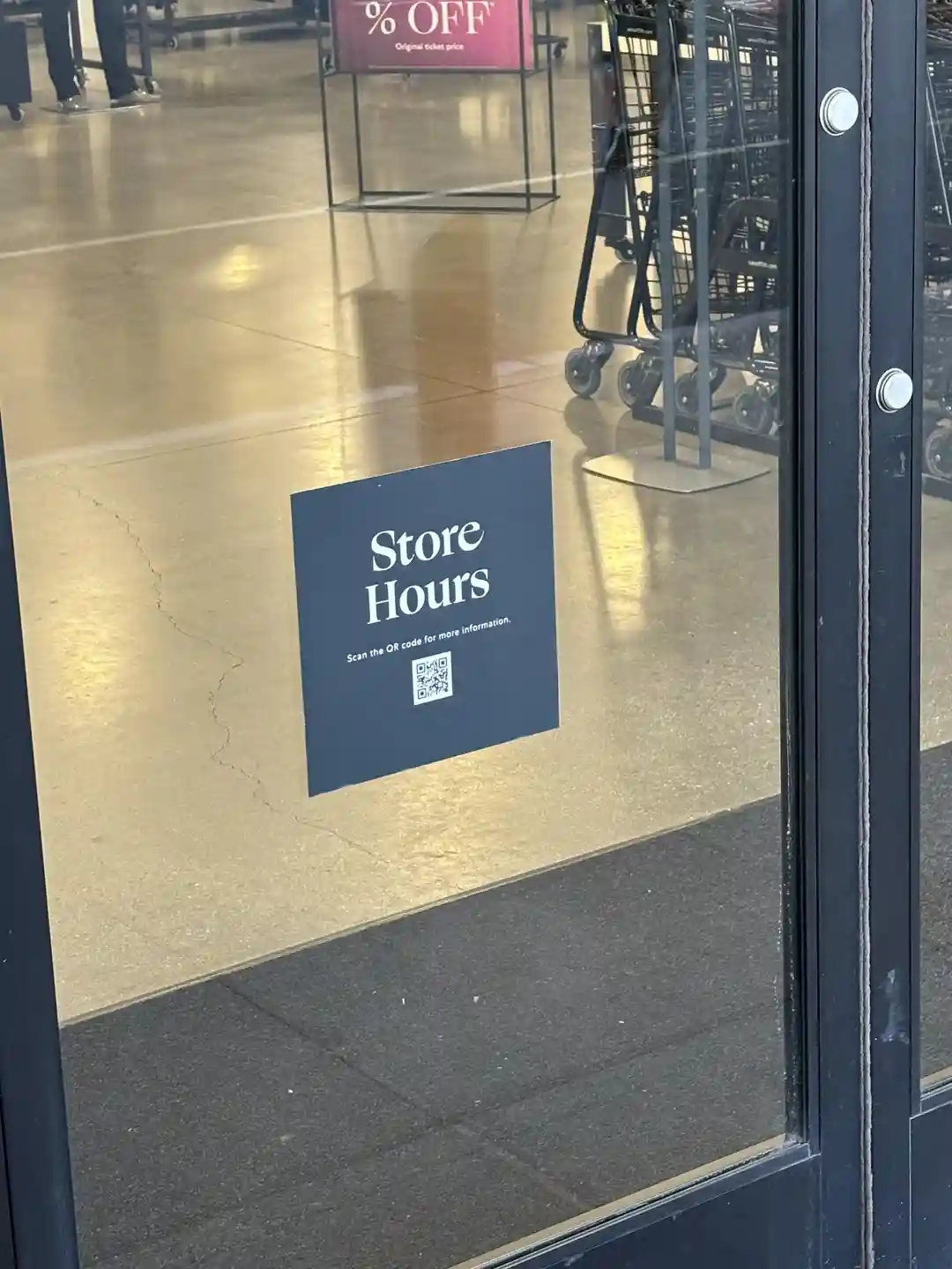 A dark blue square sign on a glass store door reads 'Store Hours' in large white text, with smaller text below saying 'Scan…