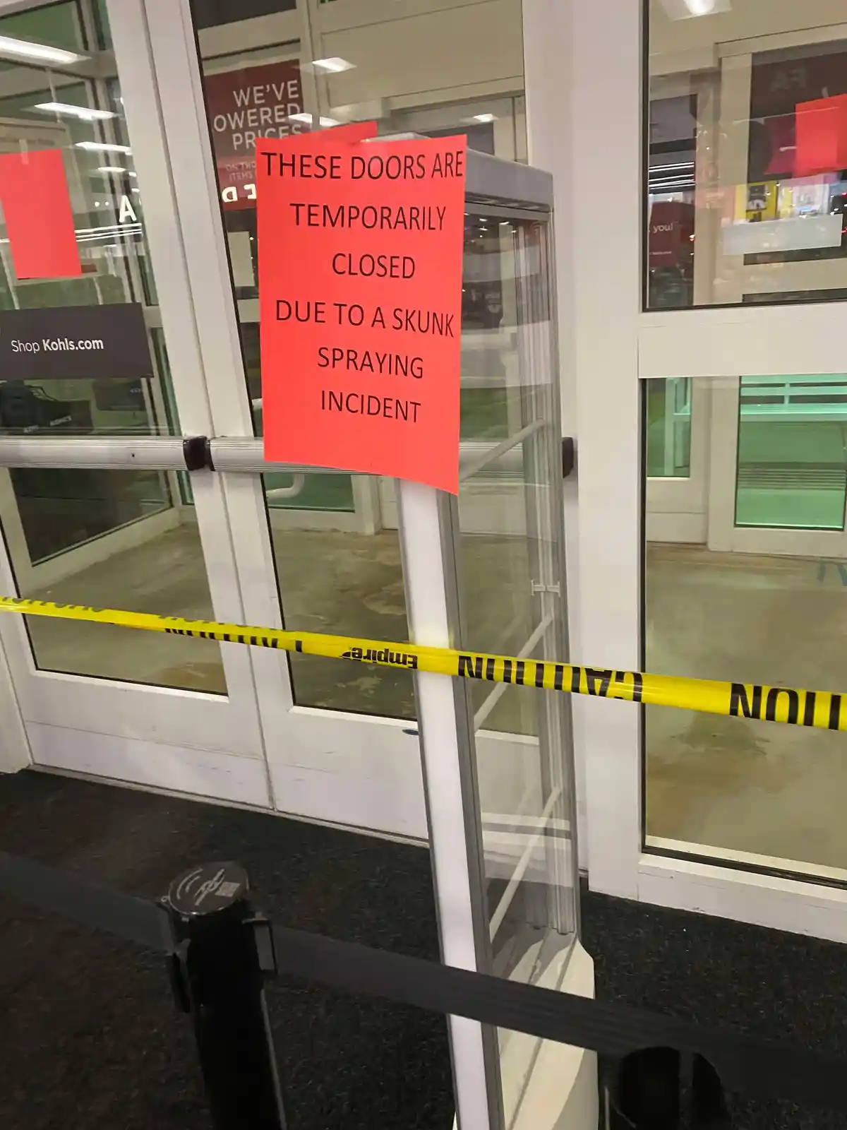 A red sign taped to glass doors at a Kohls store declares the doors are temporarily closed due to a skunk spraying incident…