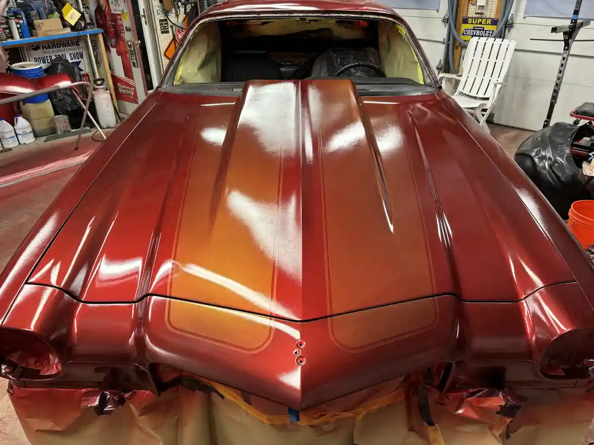 a close-up photo of a classic muscle car's hood, freshly painted with a glossy gradient of red to orange, showing spray…