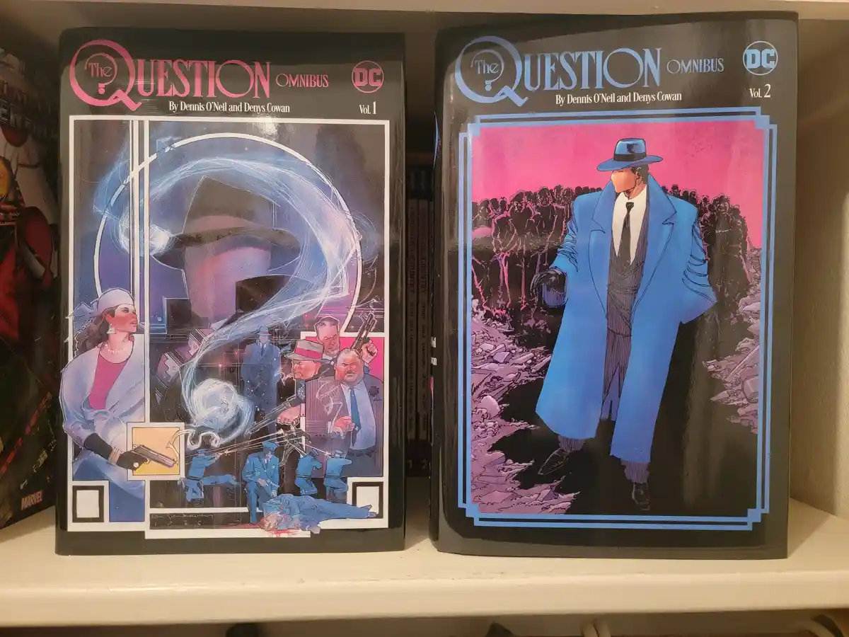 Two DC Comics 'The Question Omnibus' volumes sit side-by-side on a shelf. Volume 1 features a dynamic, multi-panel cover…
