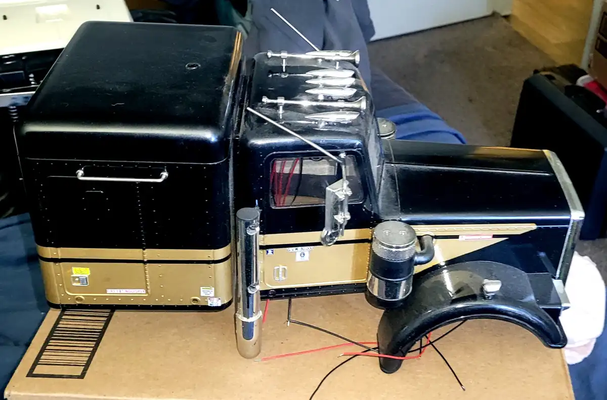 A black and gold vintage-style truck model with chrome details sits on a cardboard box, featuring a label that reads 'bird…