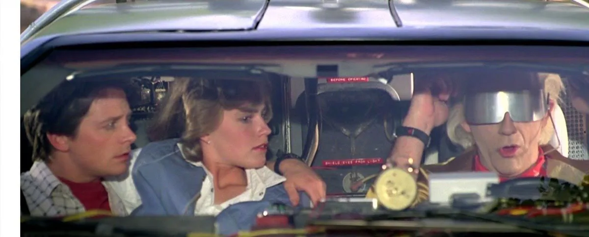 A still from the movie 'Back to the Future' shows three characters in a car: a man in a plaid shirt, a woman in a denim…