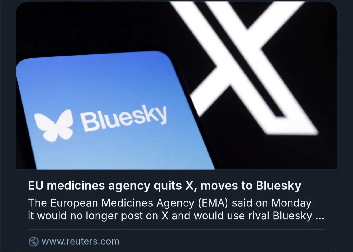 A close-up image shows a smartphone screen displaying the Bluesky app logo, which features a white butterfly icon and the…