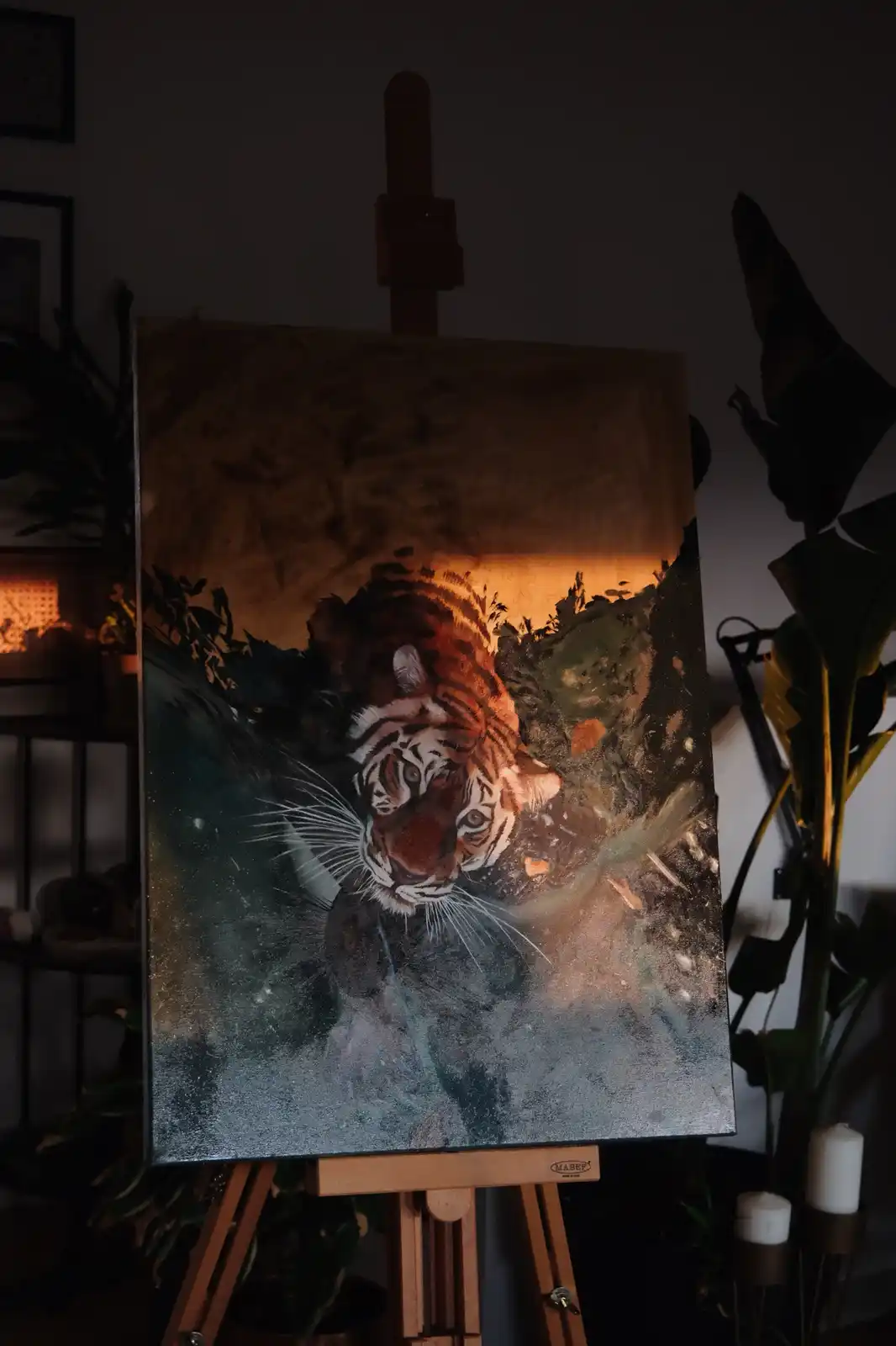 A painting of a tiger on an easel is dramatically lit from above, casting a warm glow on the tiger's face while the rest of…