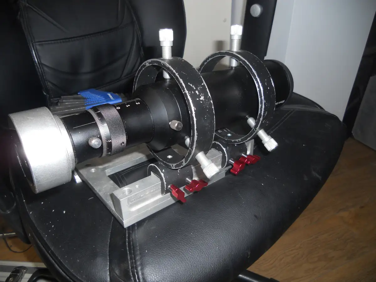 A homemade telescope mount, constructed from metal brackets, rings, and adjustment knobs, is mounted on the seat of a black…