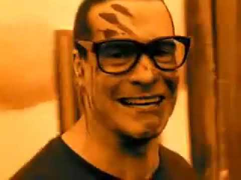 A man with dark-rimmed glasses and a wide, toothy grin has brown leaf-shaped marks on his forehead and cheeks. The image has…