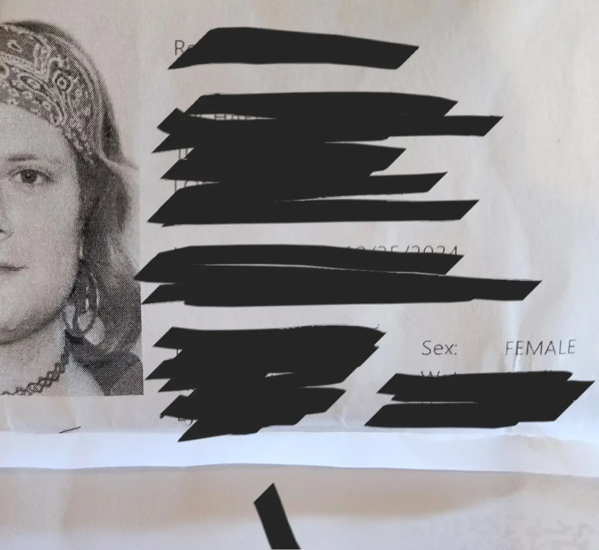A close-up of a document, likely an ID or form, showing a black-and-white photo of a woman wearing a bandana and earrings…