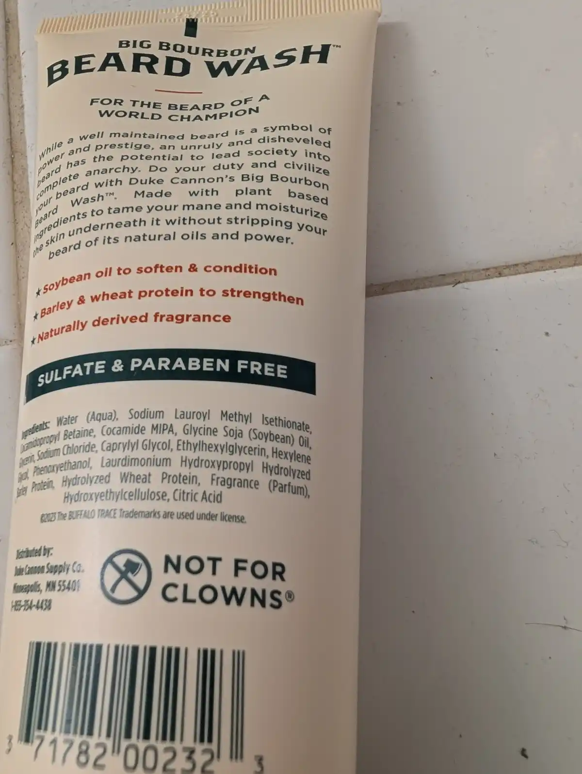 A close-up of a tube of 'Big Bourbon Beard Wash' showing its back label with product description, ingredients, and a 'NOT…