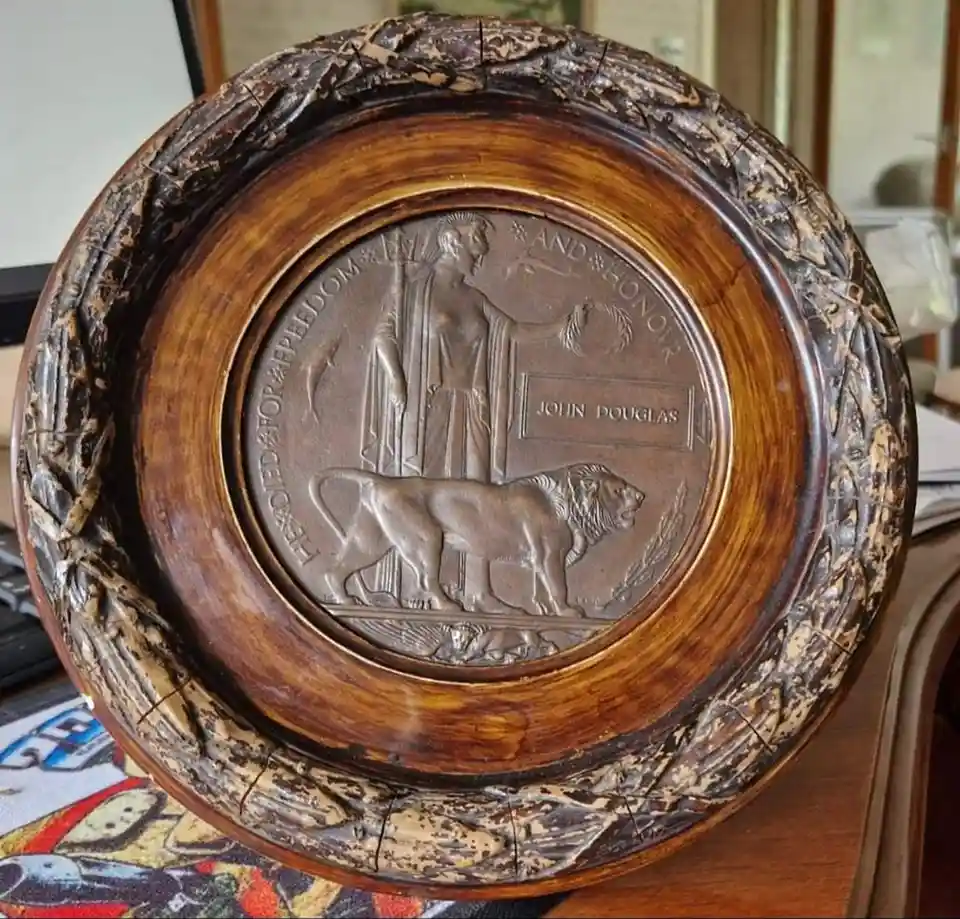 A circular wooden plaque with a bronze relief showing a standing figure holding a laurel wreath and a lion at its feet. The…