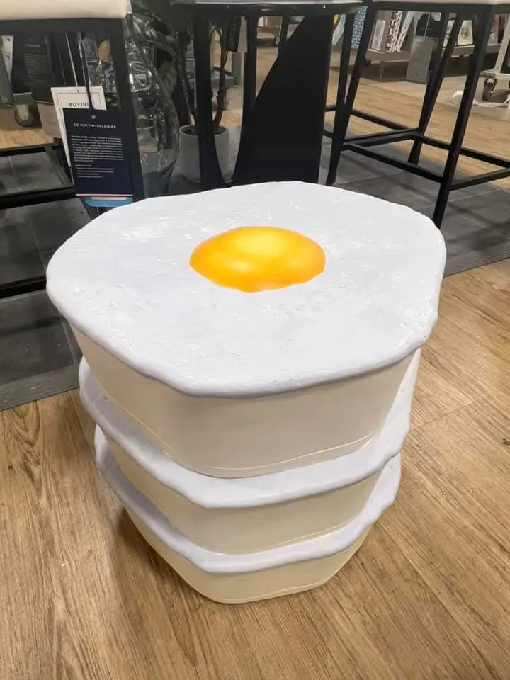 a stack of beige and white plastic-like furniture pieces shaped like a fried egg, with a yellow yolk center, displayed in a…