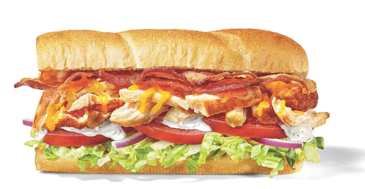 a close-up studio shot of a large chicken sandwich on a white background, featuring crispy bacon, melted yellow cheese…