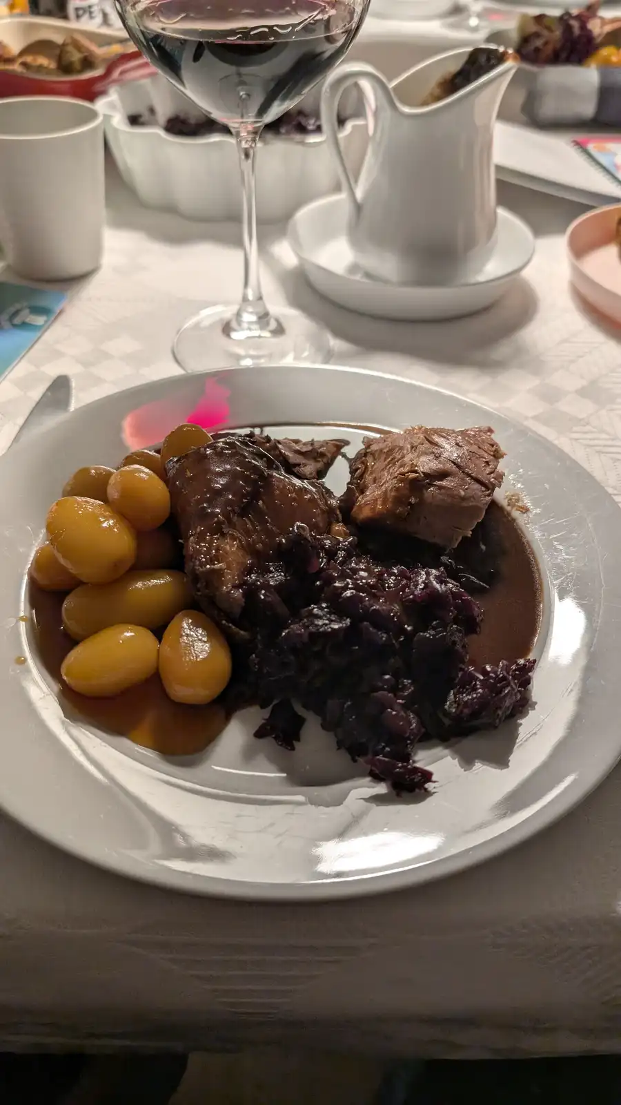 A close-up photo of a white plate holding a serving of dark meat, dark red cabbage, and yellow olives, all covered in a dark…