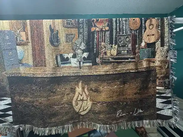 A woven tapestry depicts a cozy, retro music room with guitars, a stereo, and a vintage couch, featuring a prominent 'Chaos…