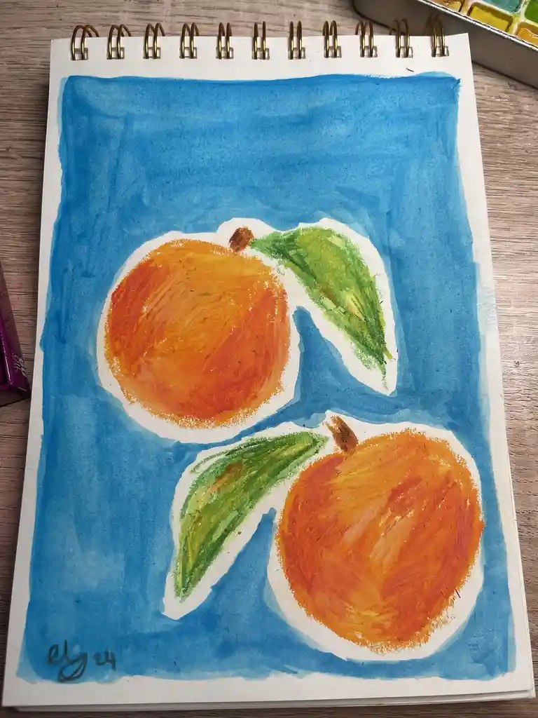 A watercolor painting on a spiral-bound sketchbook page shows two orange fruits with green leaves against a blue background…