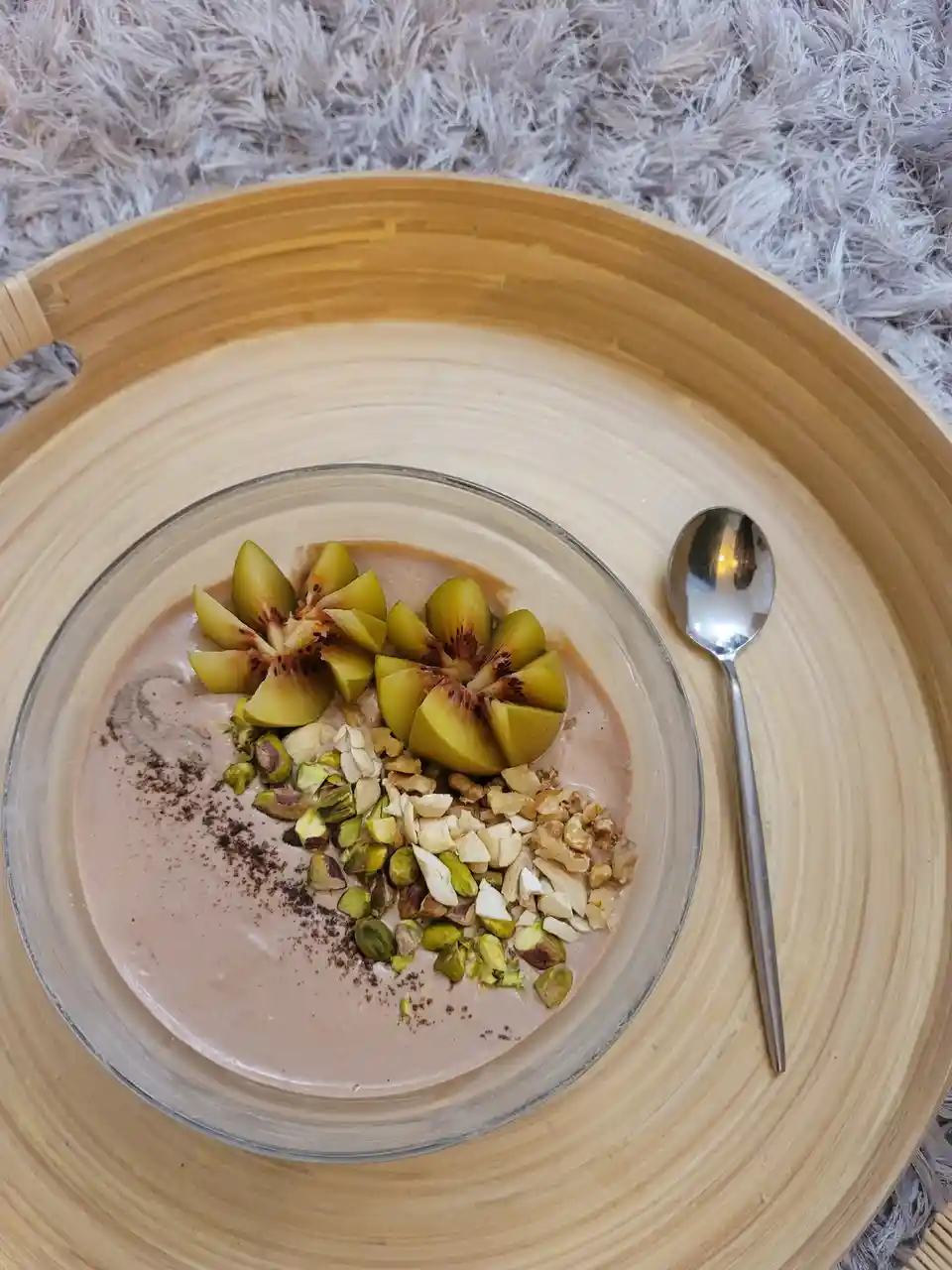 A top-down photo of a glass bowl filled with a pink smoothie or yogurt, topped with sliced figs, chopped pistachios…