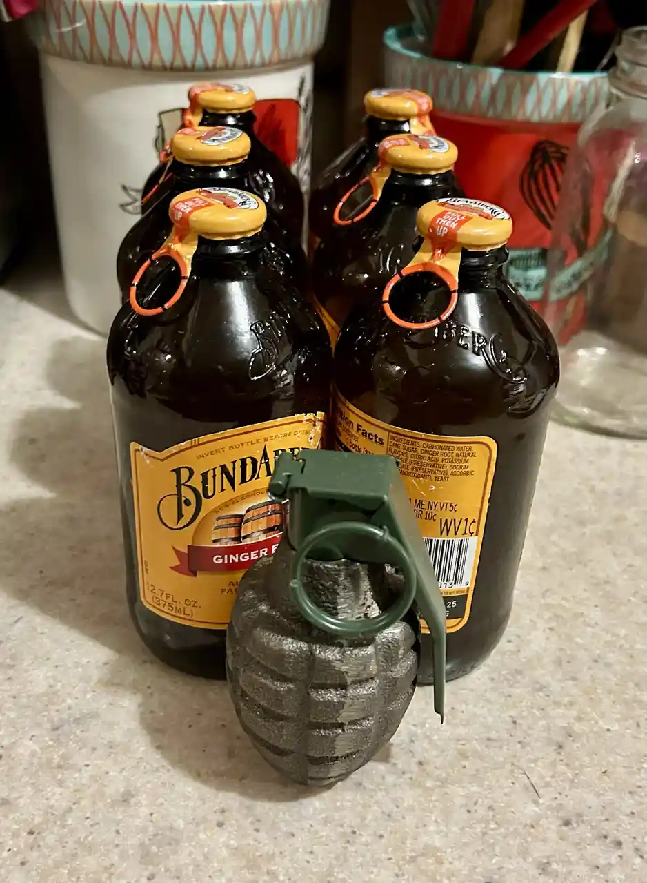 A cluster of Bundaberg ginger beer bottles sits on a kitchen counter, with a toy hand grenade placed prominently in front of…